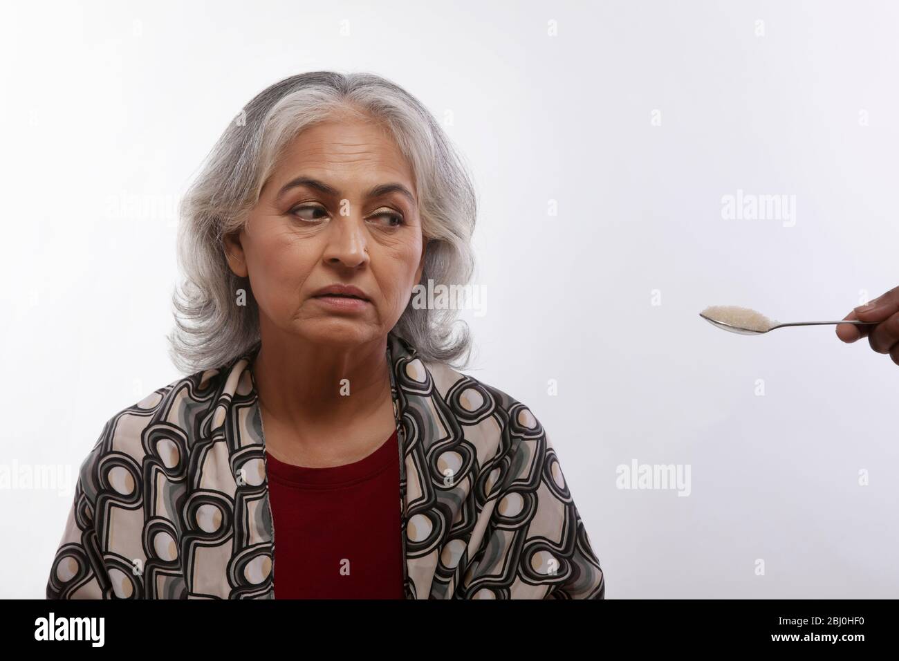 Porträt einer Großmutter, die einen Löffel Zucker ansieht. (Senior) Stockfoto