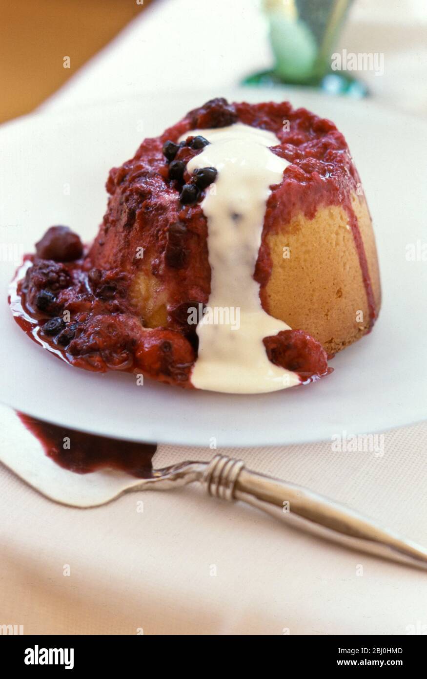 Gedämpfter Marmelade Schwammpudding auf weißem Teller, mit Sahne über gegossen - Stockfoto