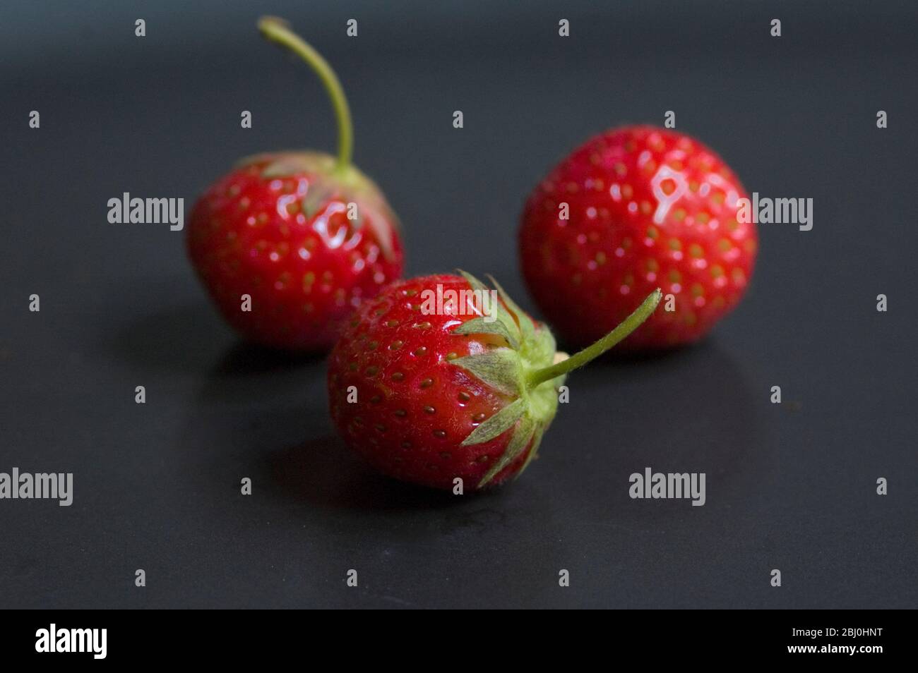 Drei kleine Erdbeeren auf einem schwarzen Teller - Stockfoto