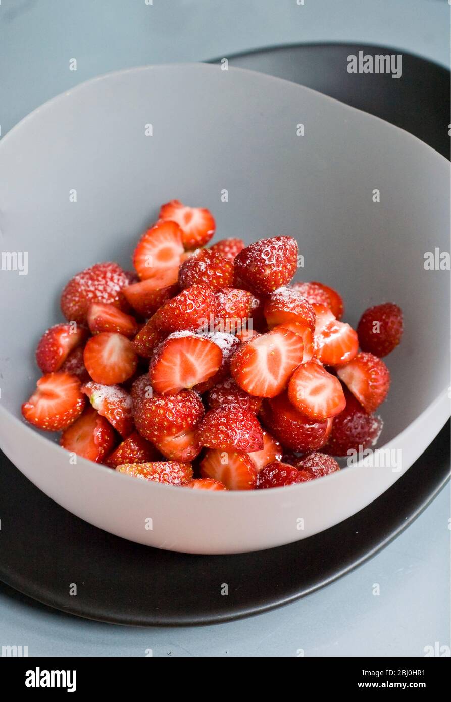 Erdbeeren, in Schüssel geschält und halbiert, mit Zucker bestäubt. - Stockfoto