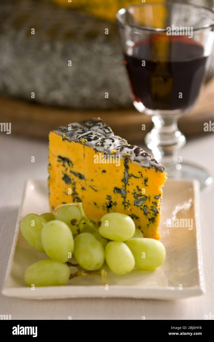 Blacksticks Blue Cheese aus Lancashire UK, serviert auf Teller mit Trauben und einem Glas Rotwein - Stockfoto