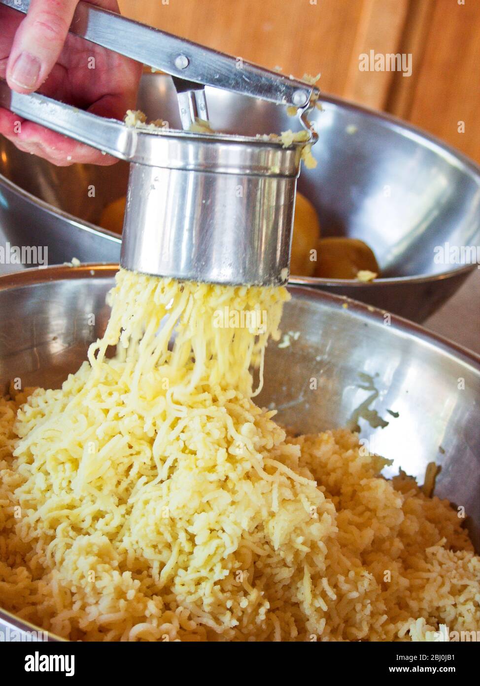 Gekochte Kartoffeln werden durch eine Kartoffelpresse gepresst, um Gnocchi zu machen - Stockfoto