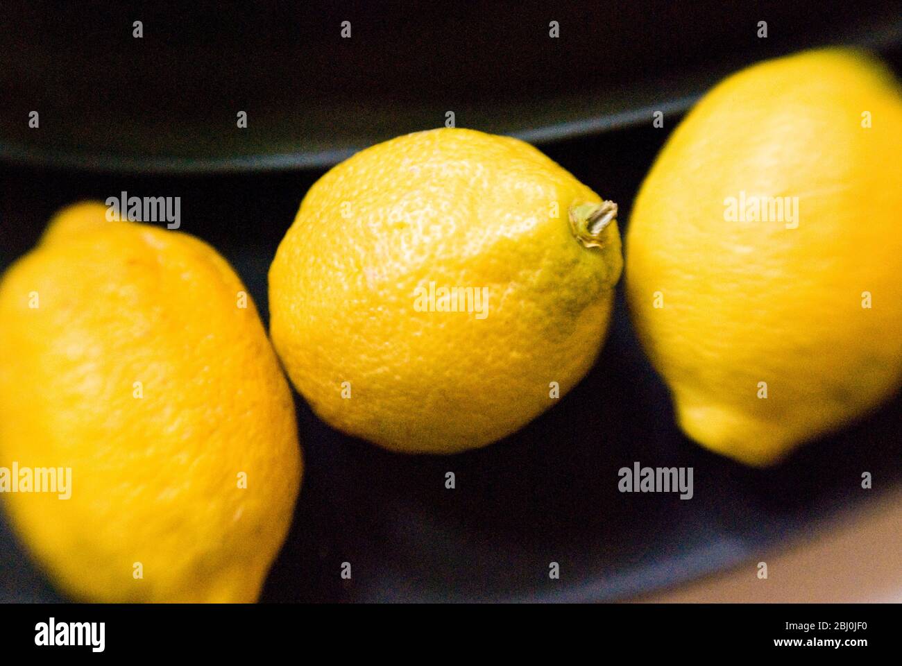 Drei Zitronen auf schwarzer Platte - aufgenommen mit einer Lenssbaby-Linse für unscharfen Rand-Effekt - Stockfoto