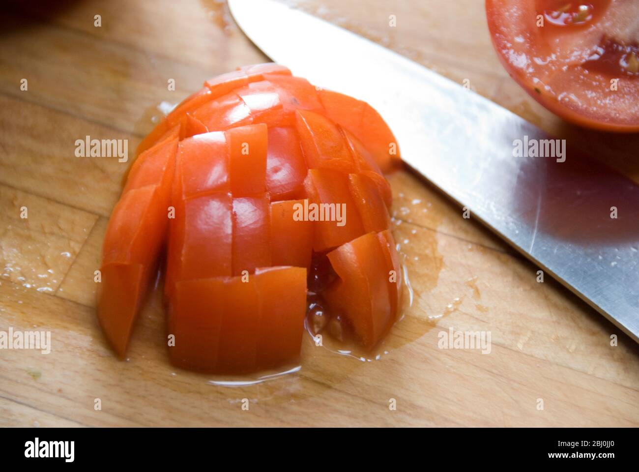 Hacken von frischen Tomaten auf Holzbrett mit scharfem Global Messer Stockfoto