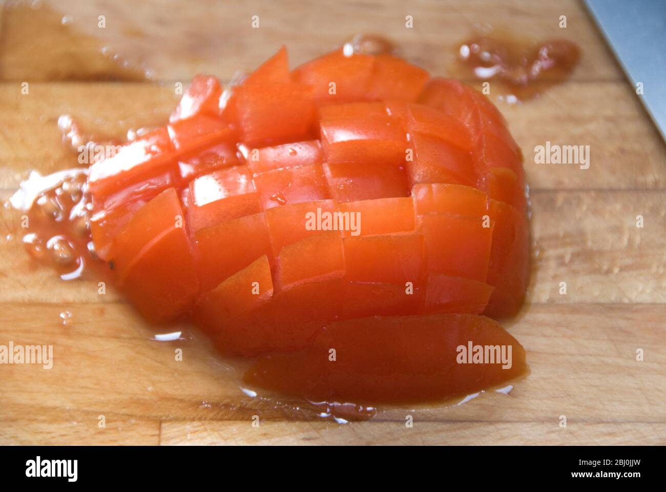 Hacken von frischen Tomaten auf Holzbrett mit scharfem Global Messer - Stockfoto