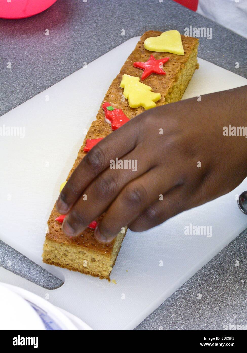 Kinder schneiden dekorative Weihnachtsformen aus farbigen Fondant Vereisung Kuchen dekorieren - Stockfoto