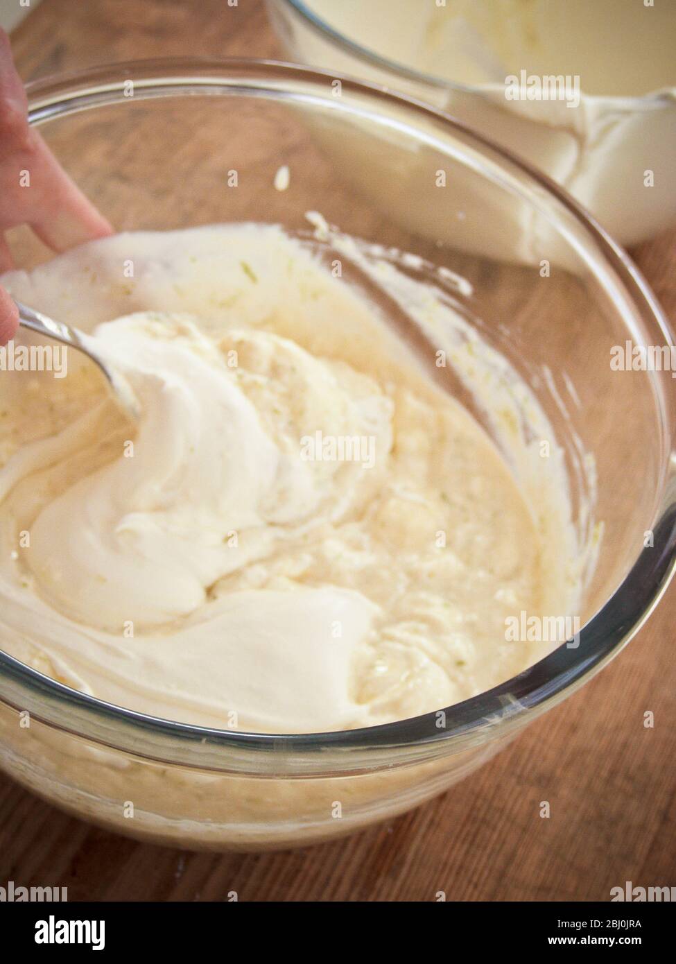 Schlagsahne in gekühlte und verdickte Eiercreme mit Gelatine und Limettenschale für ein Kleindessert mischen. - Stockfoto