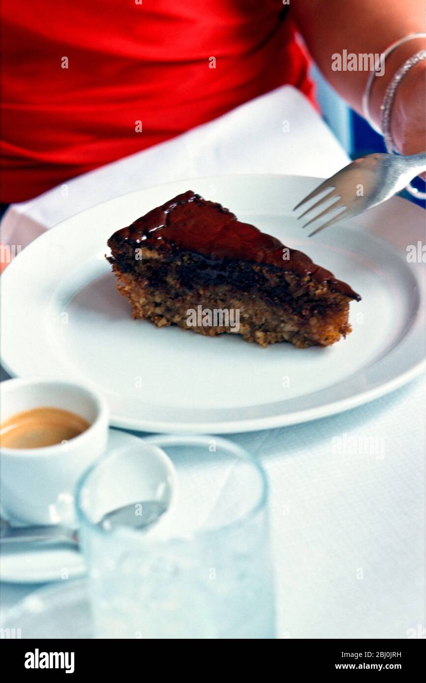 Chocolale Torte auf weißem Teller im Restaurant-Setting mit Mädchen in rotem Kleid - Stockfoto