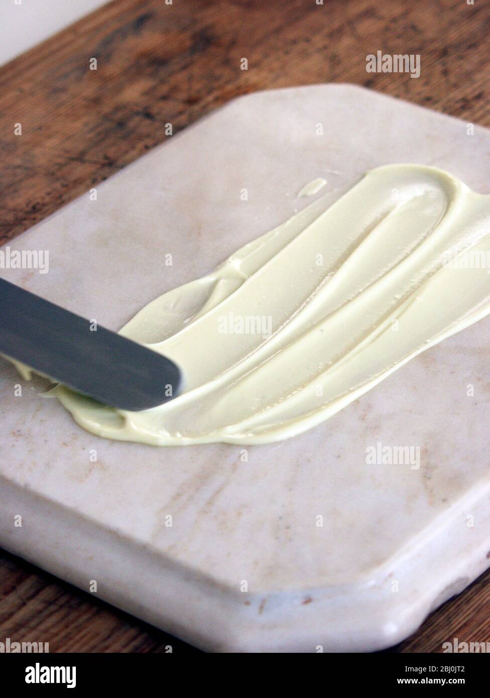 Weiße Schokolade auf Marmorplatte verteilen, um Schoko zu machen; Locken zu verlocken - Stockfoto