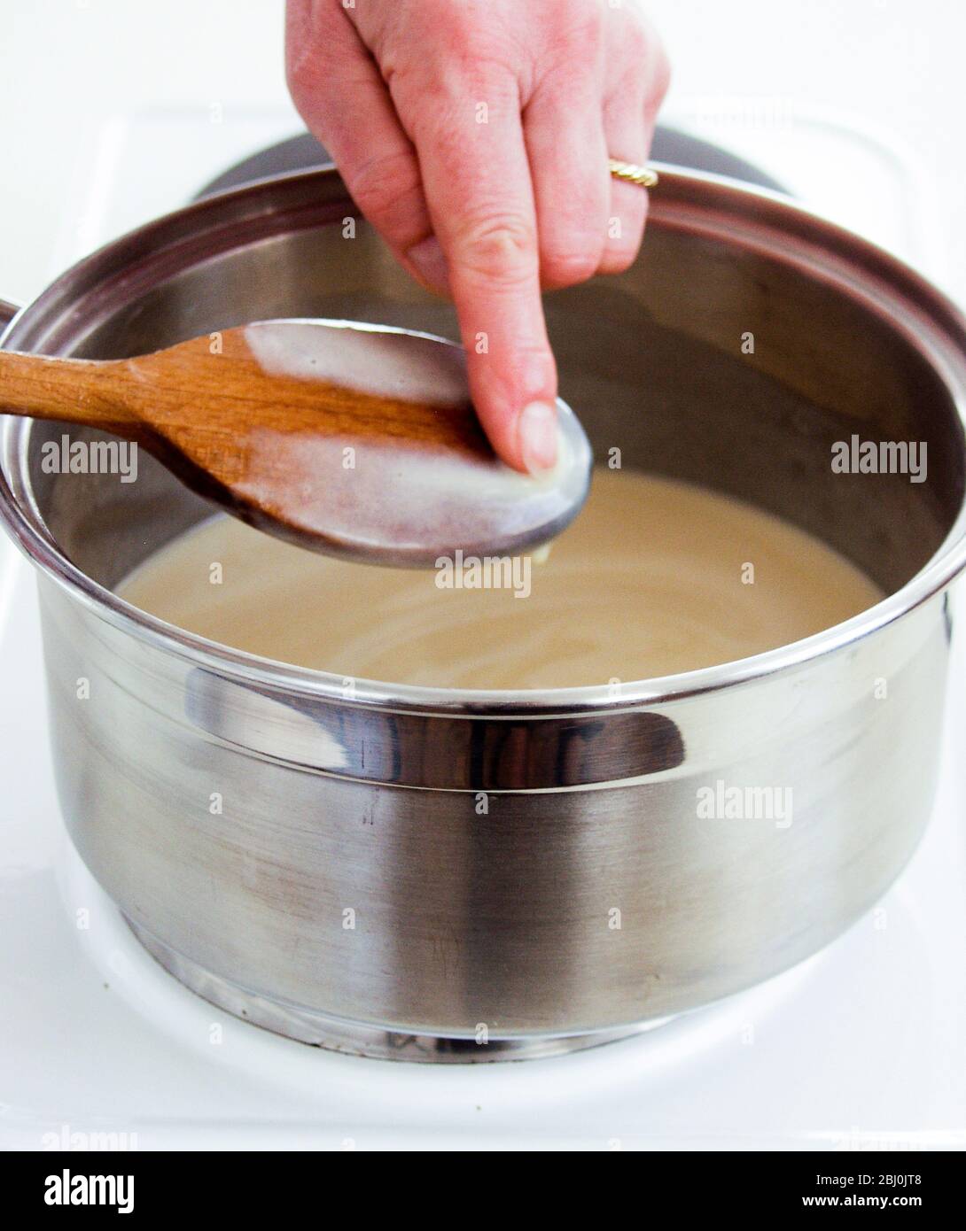 Überprüfen der Dicke eines Pudding, indem Sie sehen, wie gut es die Rückseite eines Löffels umhüllt - Stockfoto