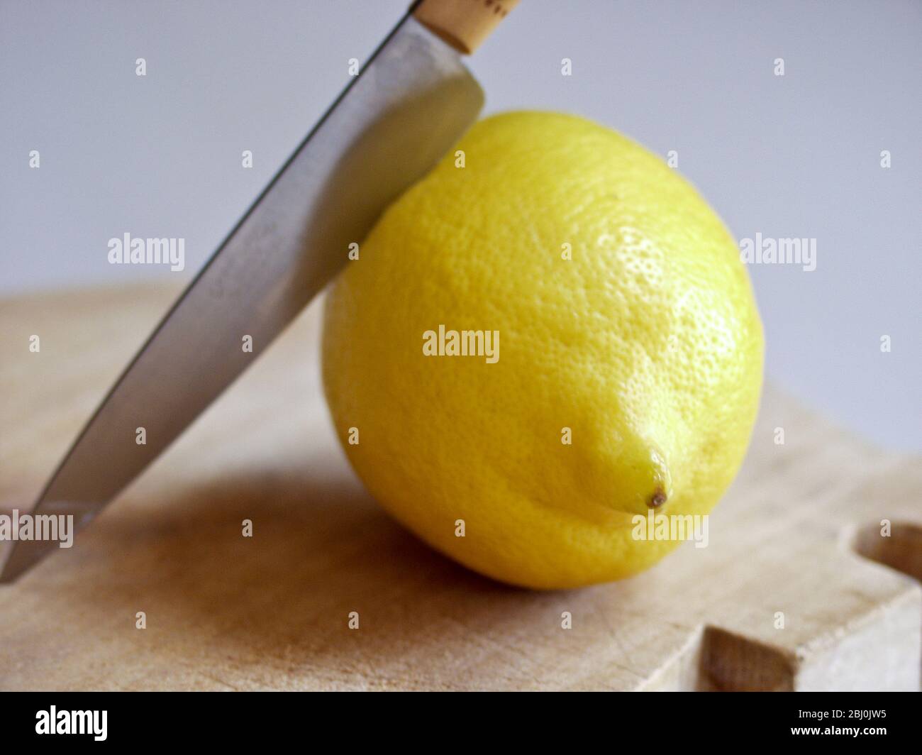 Ganze frische Zitrone mit Messer auf Schneidebrett - Stockfoto