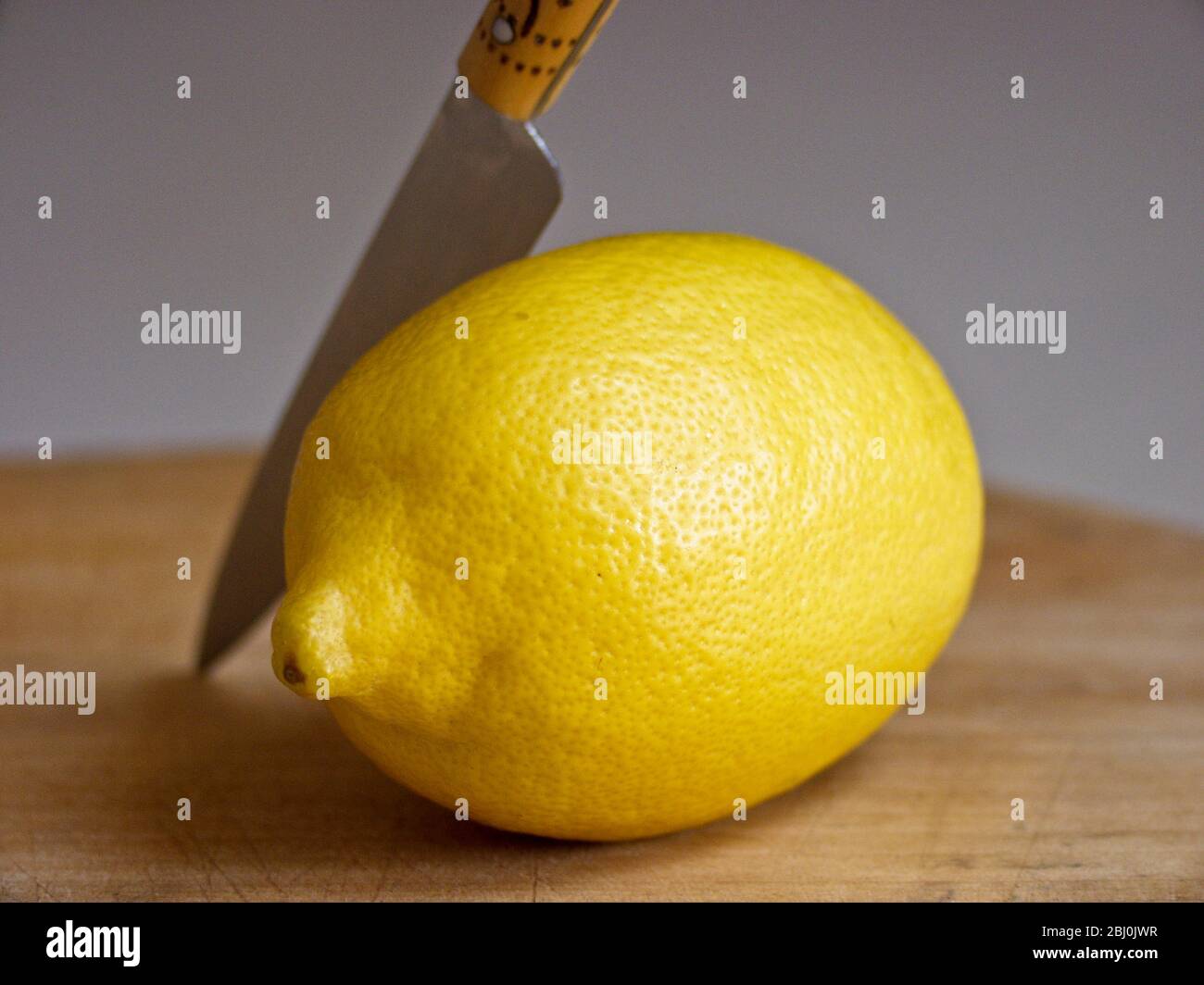 Ganze frische Zitrone mit Messer auf Schneidebrett - Stockfoto