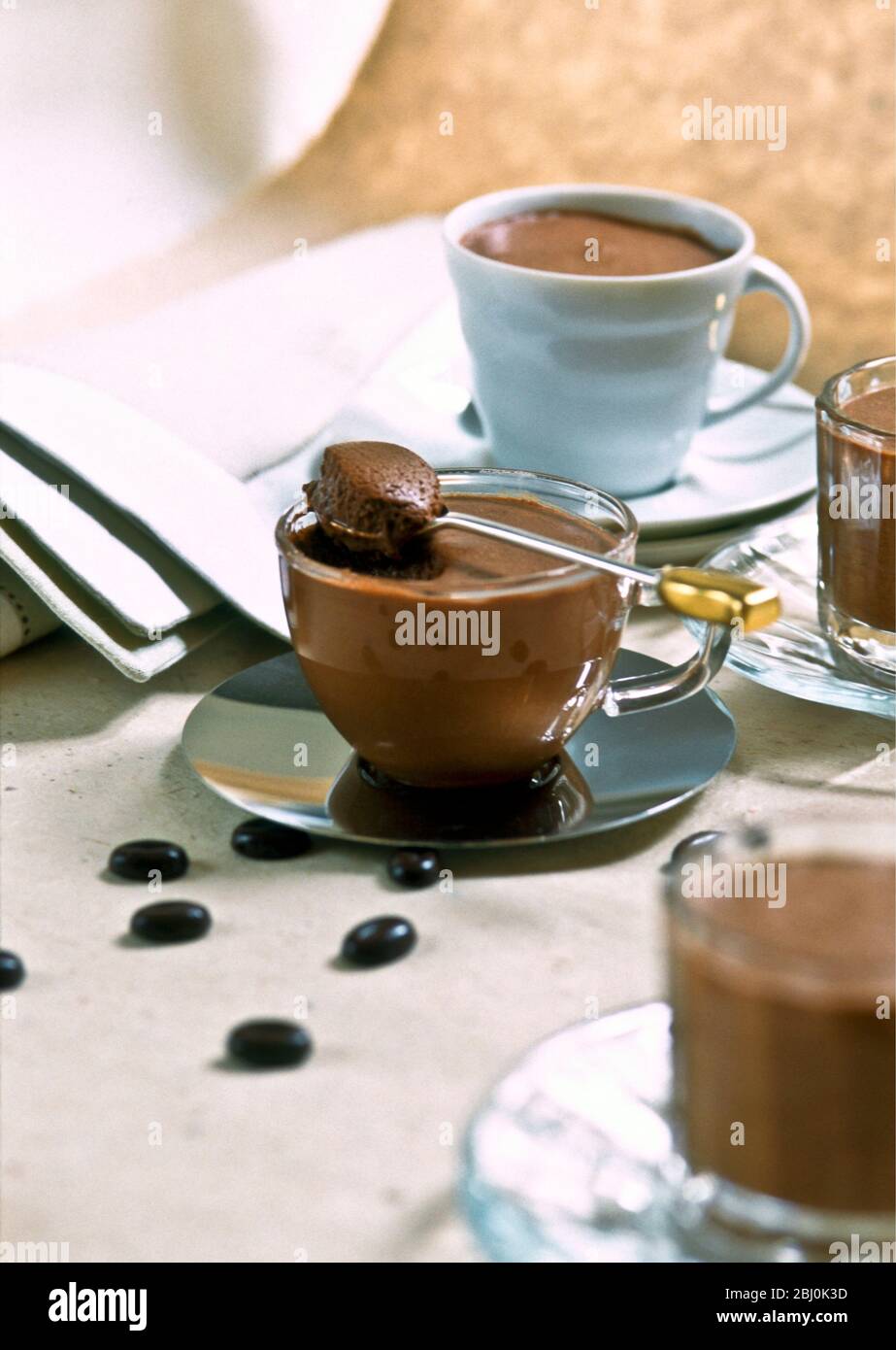 Schokoladenmousse in einer Vielzahl von hübschen Tassen mit Kaffeebohnenschokolade auf dem Tisch verteilt serviert - Stockfoto
