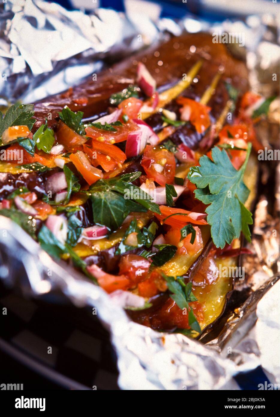 Ganze Aubergine in fächerförmige Form mit rohen gehackten Tomaten, Koriander, Petersilie, rote Zwiebel und Olivenöl schneiden, bevor sie in Folienverpackung versiegelt und kochen Stockfoto