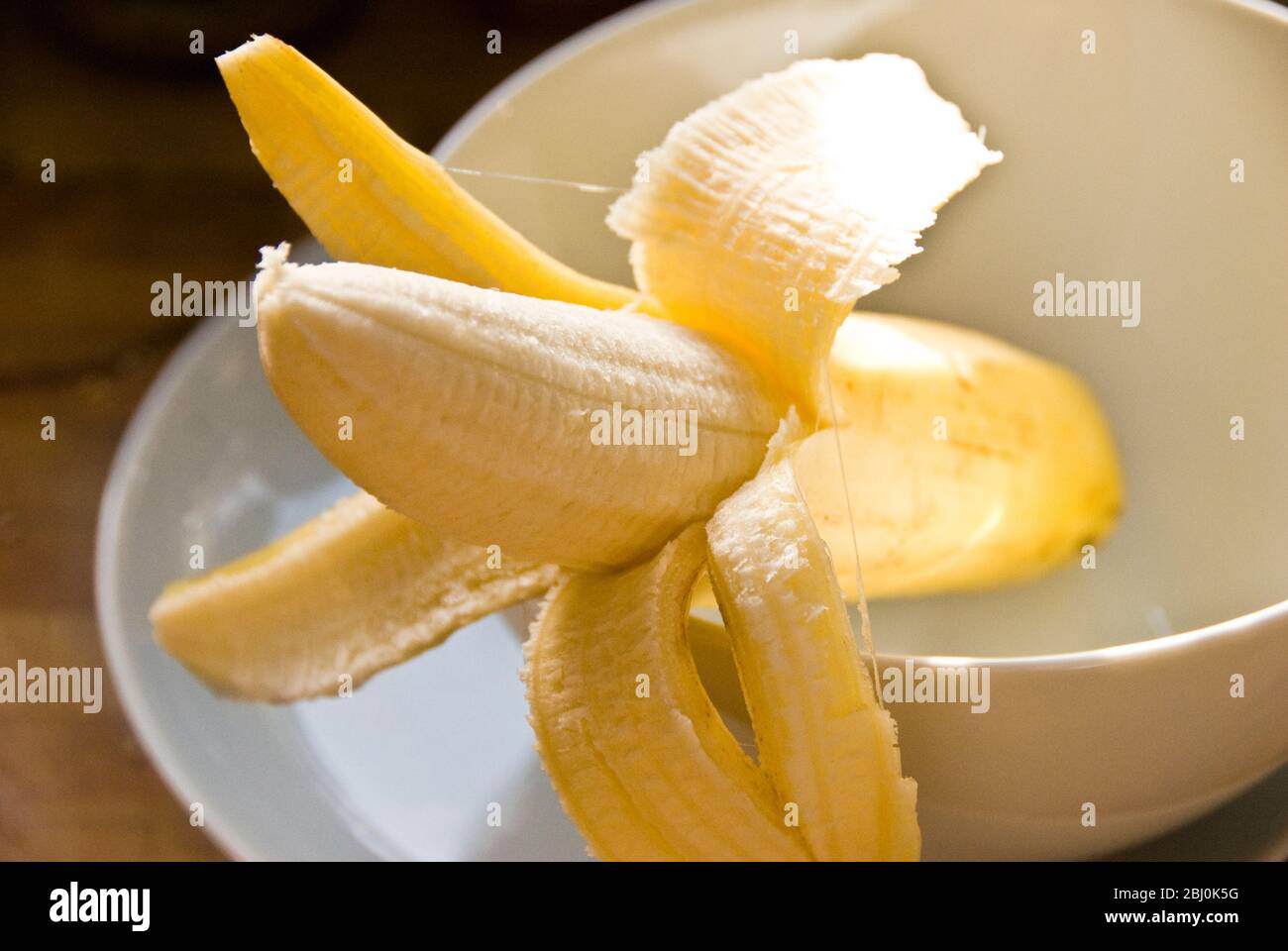 Halbgeschälte Banane in weißer Schale - Stockfoto
