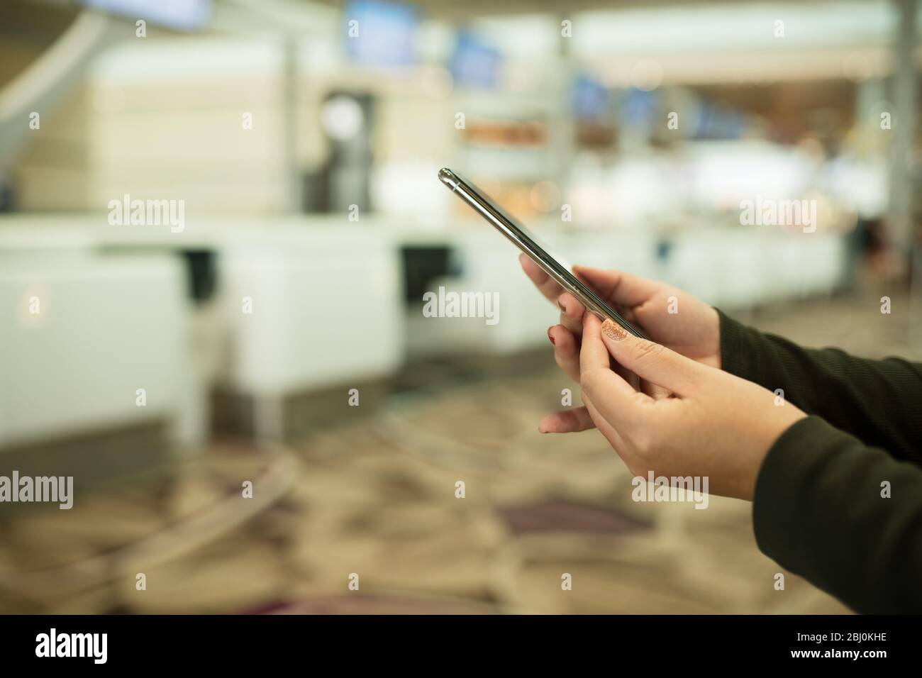 Menschen Hände benutzen Handy am Schalter Check-in Flughafen im Hintergrund mit Bokeh, überprüfen Flugnummer auf Handy im Flughafen Stockfoto