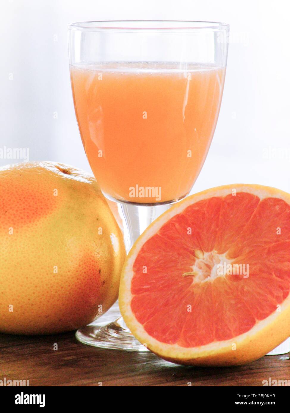 Frische ganze rosa Grapefruits mit einem Glas Grapefruitsaft - Stockfoto