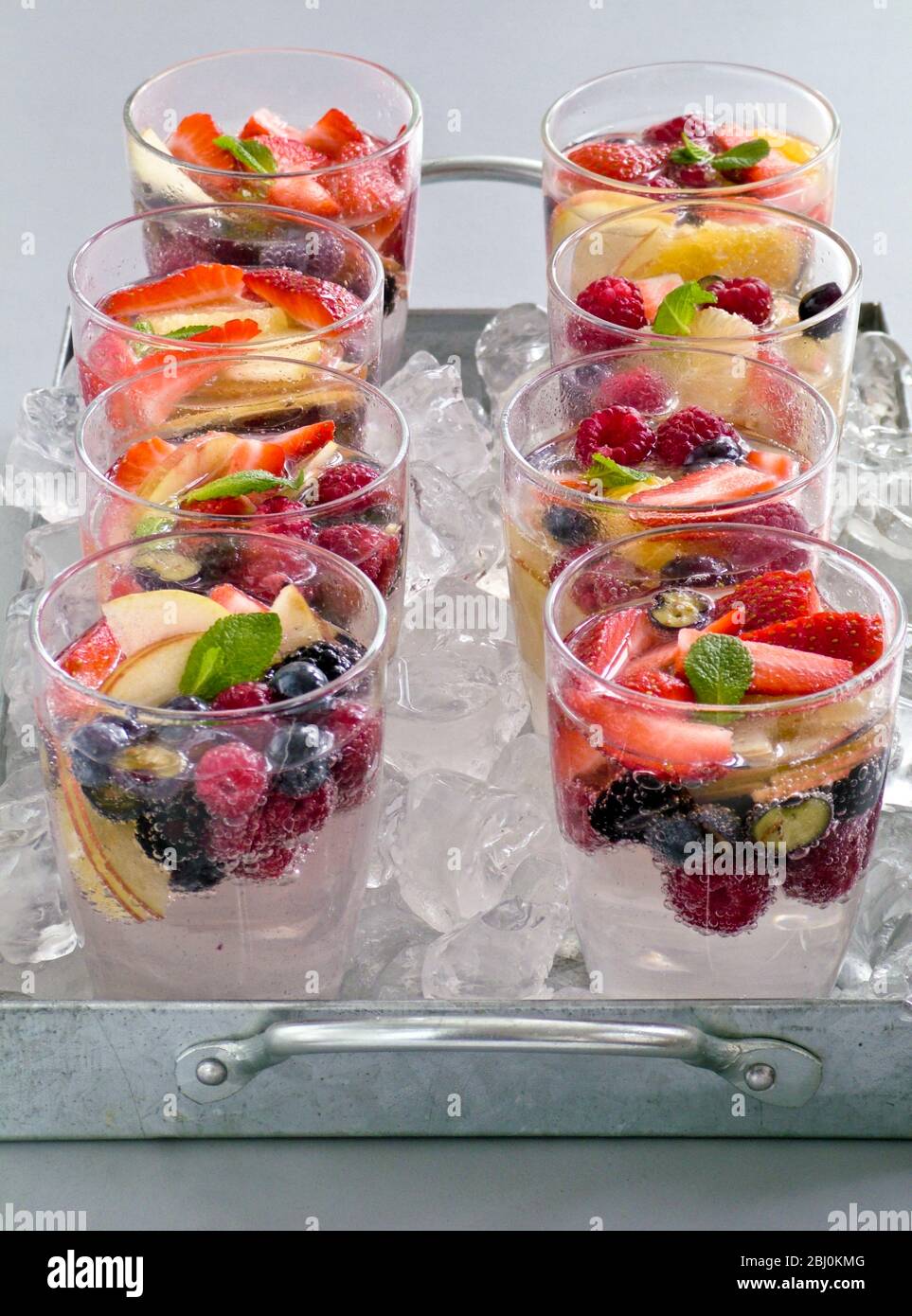 Mineralwasser mit frischem Obst und Beeren in Gläsern Sittin gon zerkleinerten Eis auf Metallschale. - Stockfoto