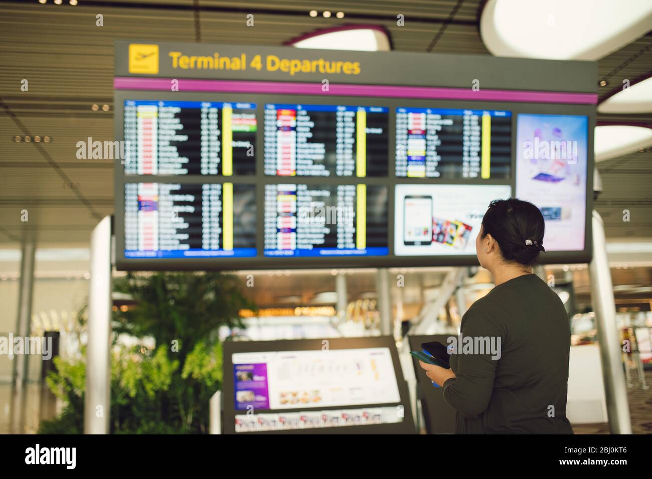 Passagiere, die am Fluginformationsbrett im Wartebereich des Flughafenterminals reisen, prüfen die Zeit für Abflug-Ankunft und den Flugstatus für Verspätungen Stockfoto