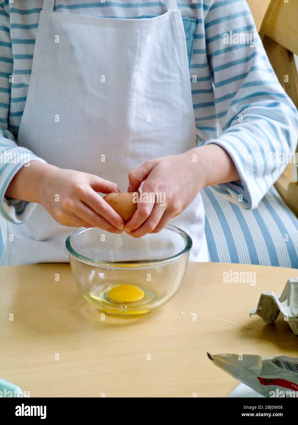 Kind bricht Eier in Glasschüssel, lernen, wie man Rührei machen. - Stockfoto