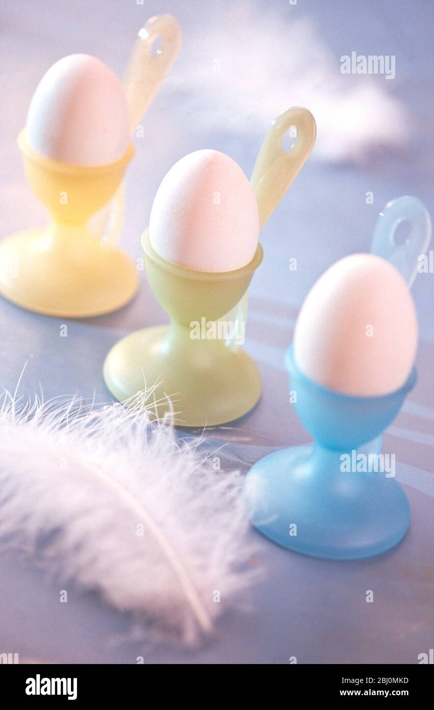 Pastellfarbene Eierbecher mit gekochten Eiern und Federschmuck - Stockfoto