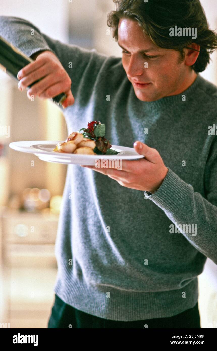 James Martin, TV-Chef, nieselndes Olivenöl über Gericht gebratene Jakobsmuscheln mit gemischten Salatblättern garnieren - Stockfoto