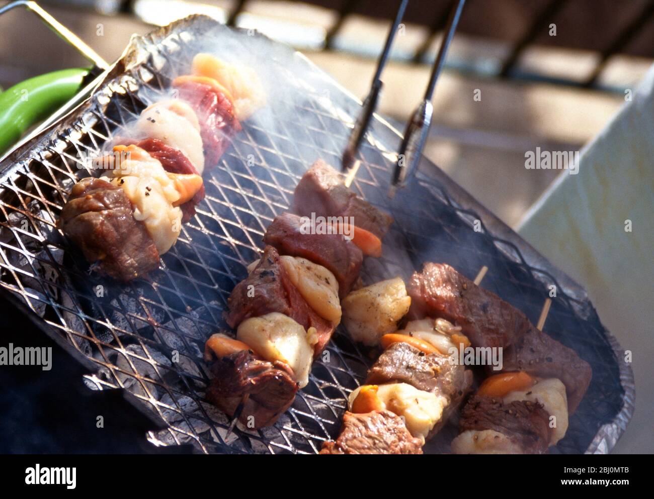 Grillen von Jakobsmuscheln und Steak-Kebabs auf einem Holzkohlegrill - Stockfoto