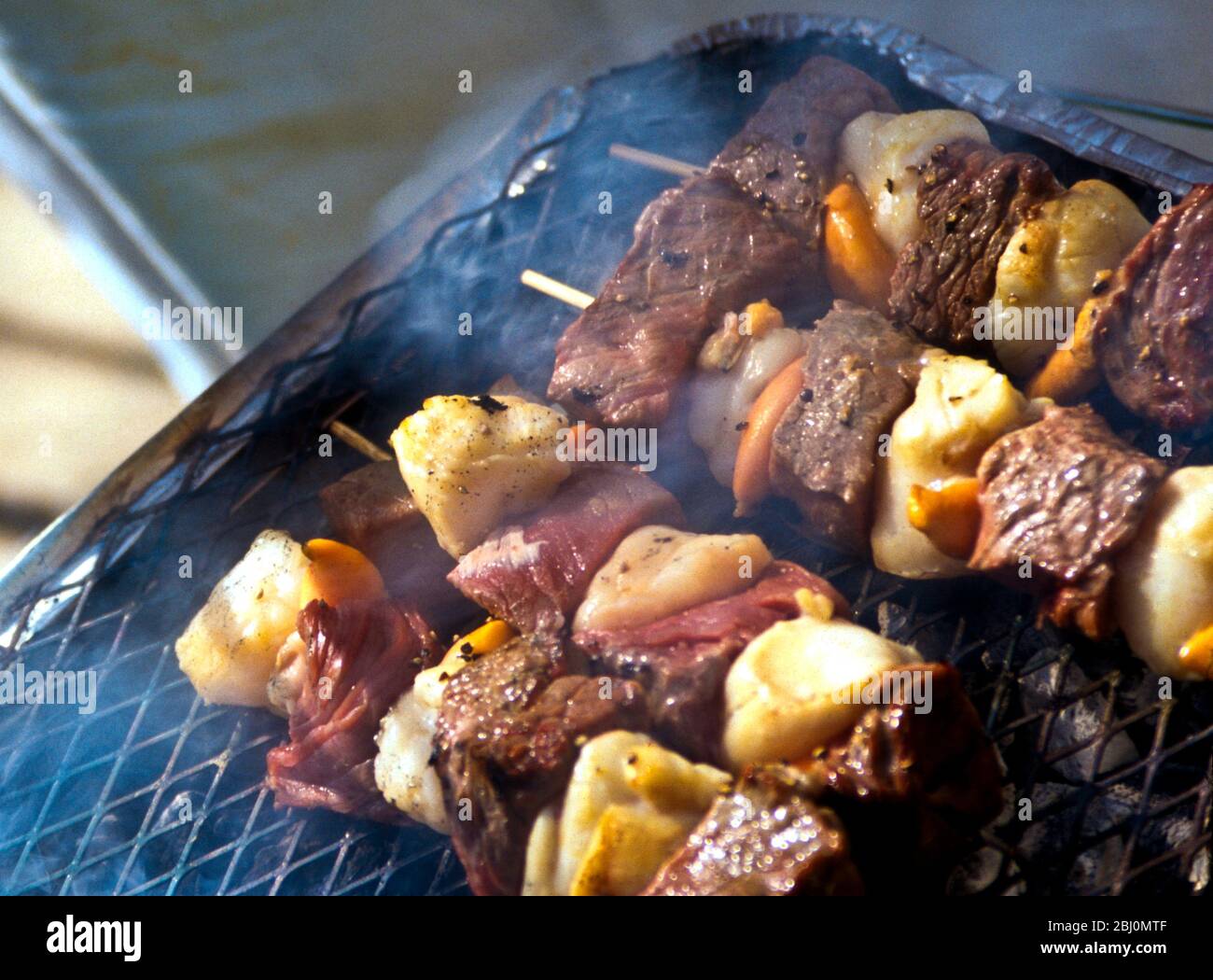 Grillen von Jakobsmuscheln und Steak-Kebabs auf einem Holzkohlegrill - Stockfoto