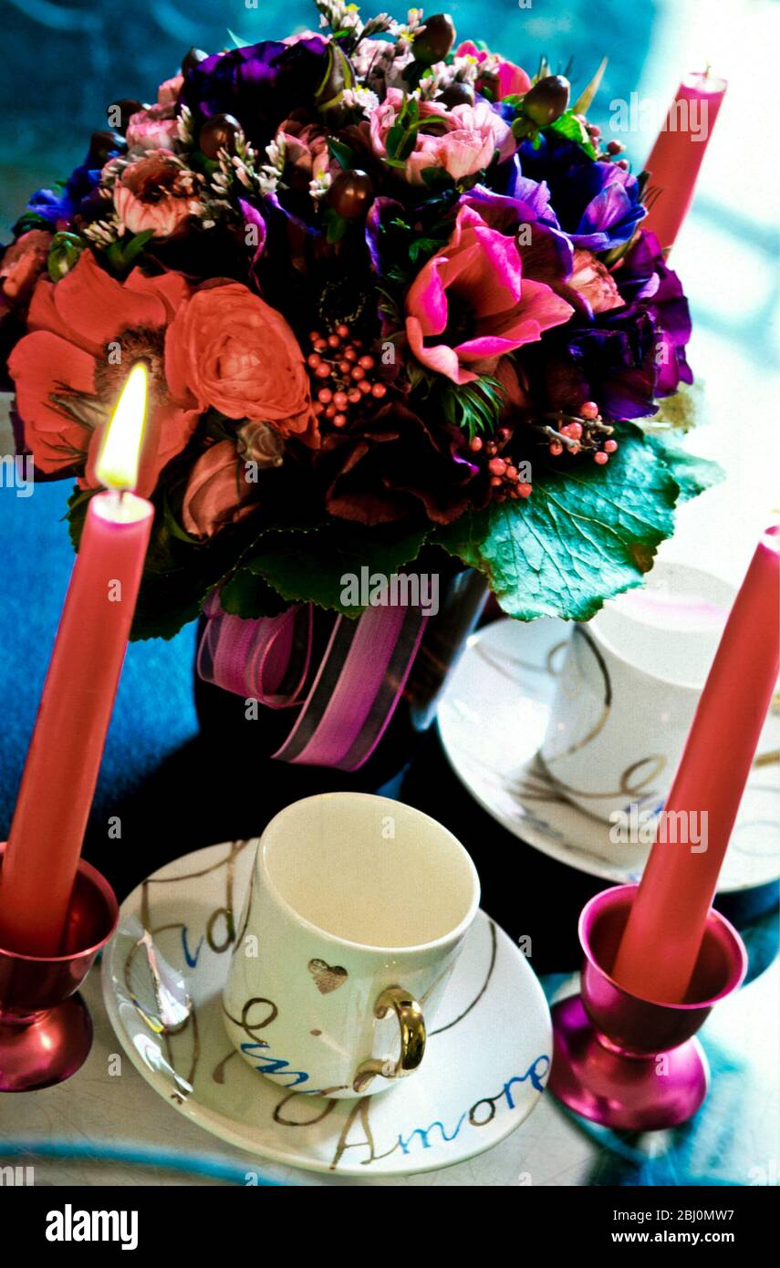 Festtischunterlage mit rosa Kerzen, goldverzierten Kaffeetassen und extravaganter Mischung aus Posy und Anemonen - Stockfoto