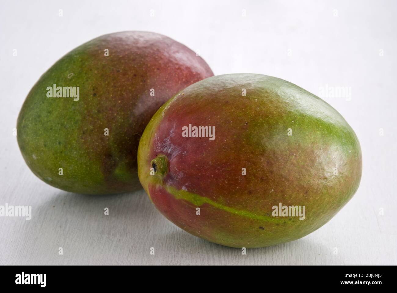 Zwei ganze Mangos auf weißer Oberfläche - Stockfoto