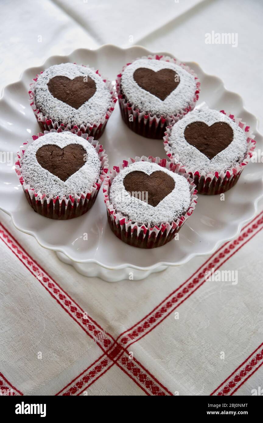 Fünf Schokoladen-Muffins mit Puderzucker in Herzform auf weißem Kuchenständer verziert - Stockfoto