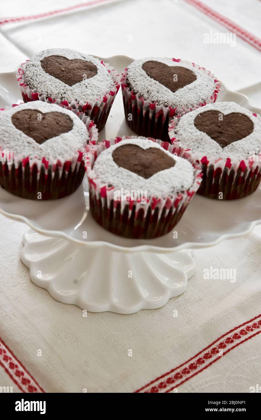 Fünf Schokoladen-Muffins mit Puderzucker in Herzform auf weißem Kuchenständer verziert - Stockfoto