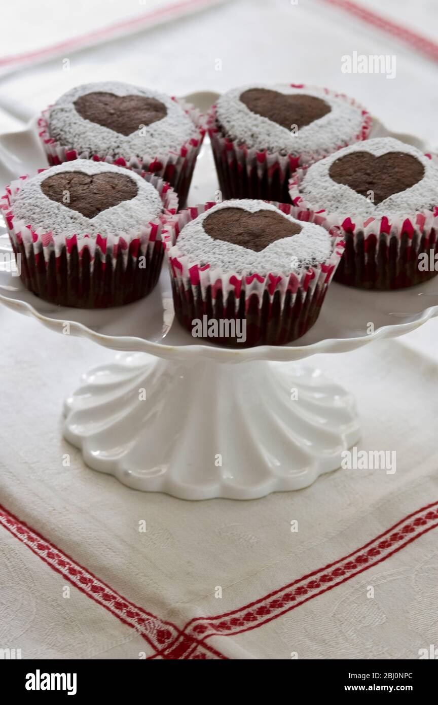 Fünf Schokoladen-Muffins mit Puderzucker in Herzform auf weißem Kuchenständer verziert - Stockfoto