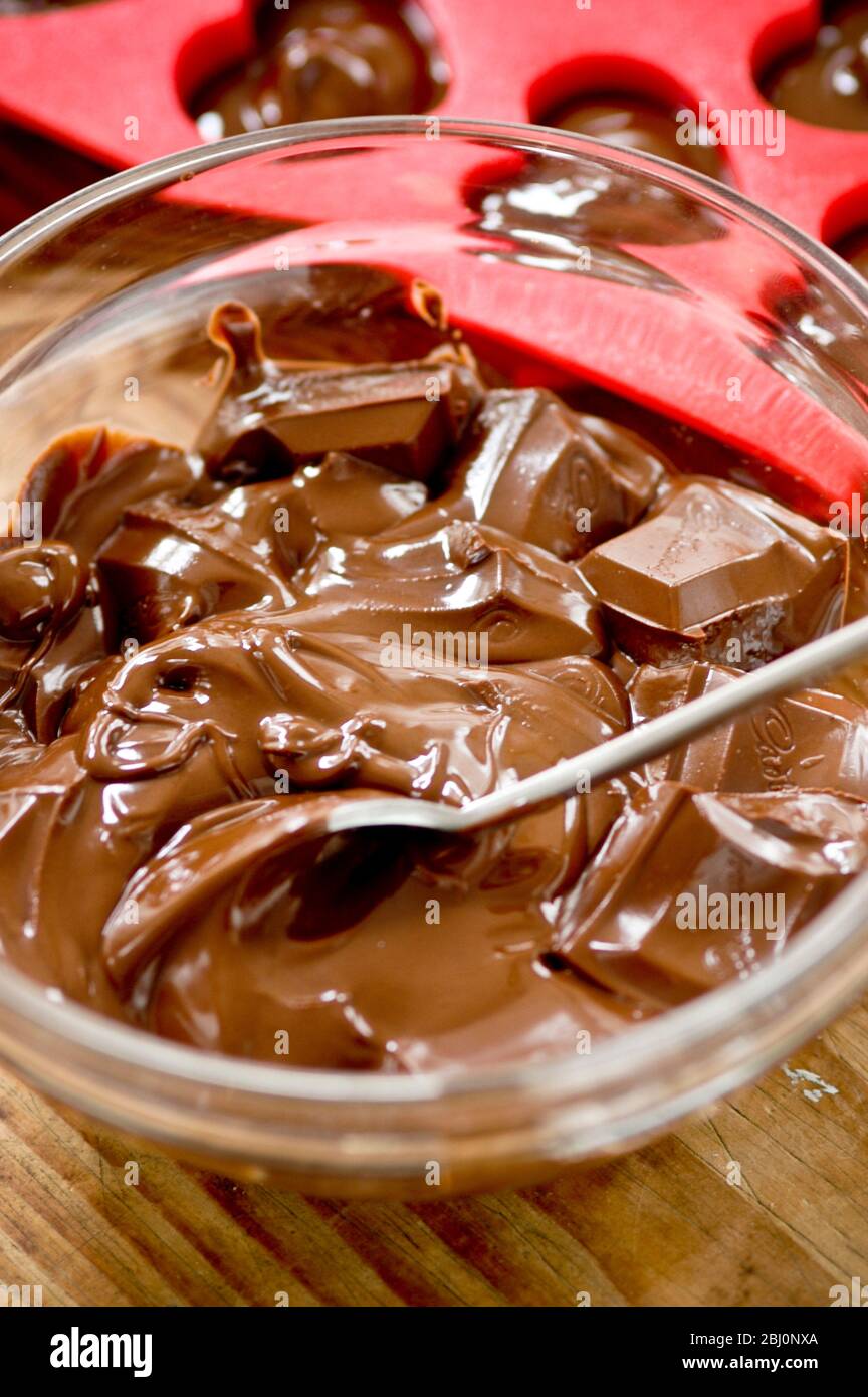 Geschmolzene Schokolade in Glasschale mit roter Herzform dahinter - Stockfoto