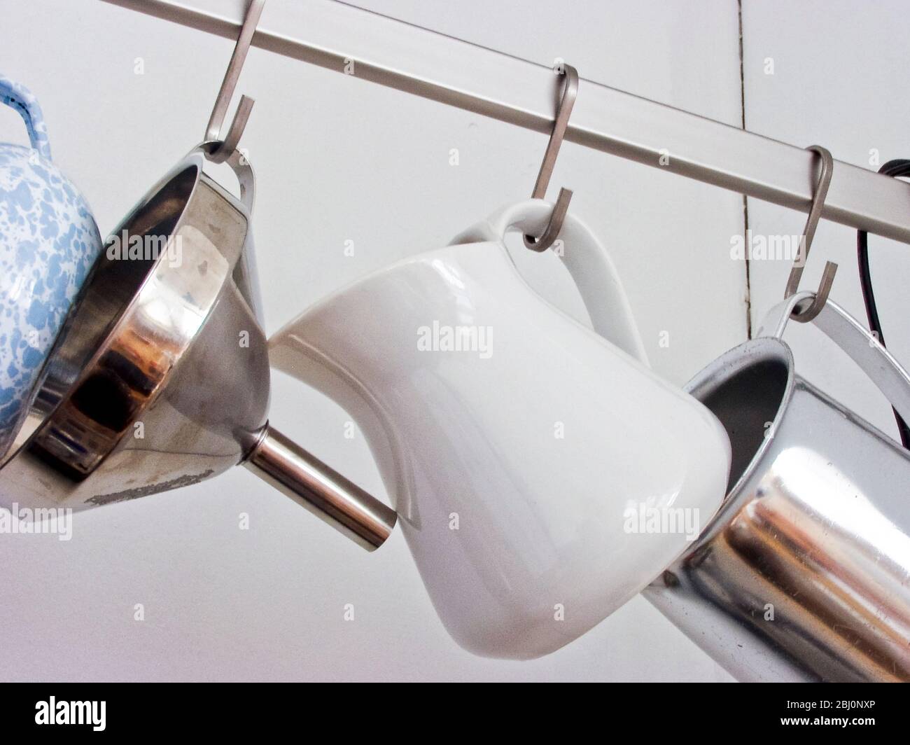 Verschiedene Küchenbecher und ein Trichter hängen an Metallschiene - Stockfoto