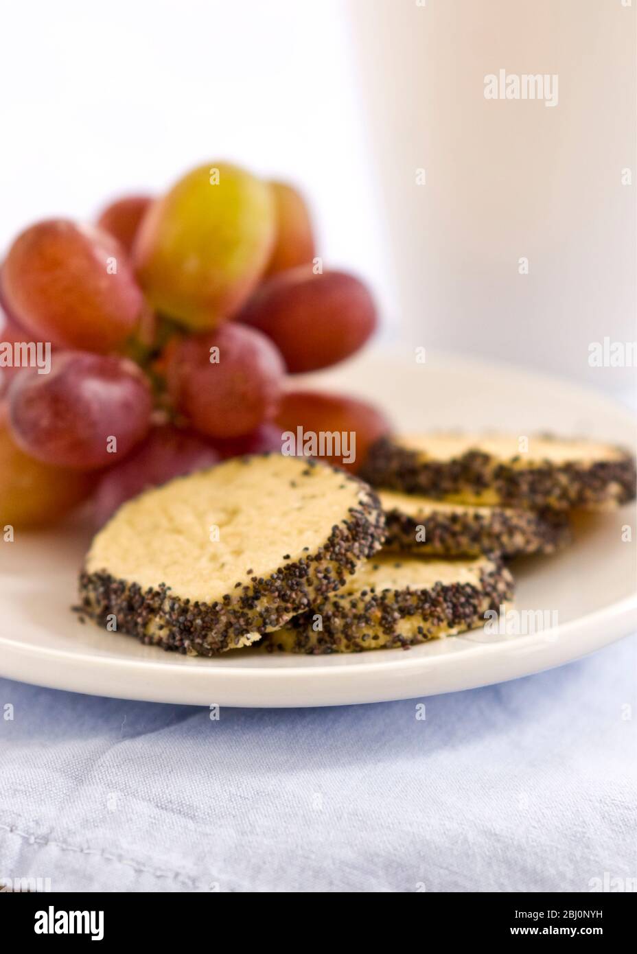 Leichter Snack oder Mahlzeit aus hausgemachtem Käsekeks mit Mohn-Rand, serviert mit roten Trauben - Stockfoto