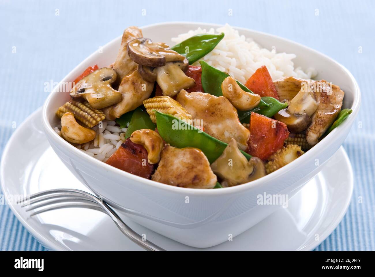 Leichtes, gesundes Gericht mit gebratenen Hähnchenstücken mit Gemüse und Cashewnüssen in chinesischer Sauce auf Reis, serviert in einer einfachen weißen Schüssel. Sh Stockfoto