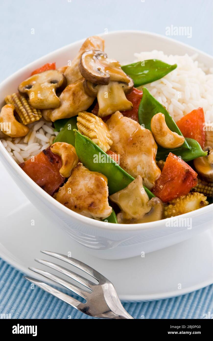 Leichtes, gesundes Gericht mit gebratenen Hähnchenstücken mit Gemüse und Cashewnüssen in chinesischer Sauce auf Reis, serviert in einer einfachen weißen Schüssel. Sh Stockfoto