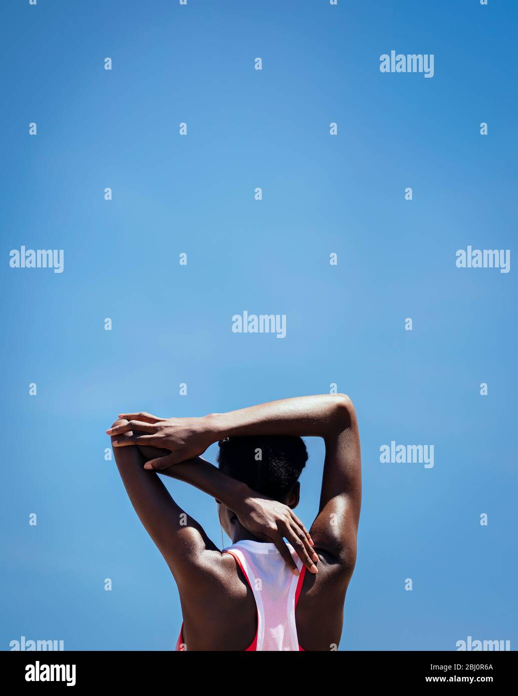 Rückansicht einer Frau, die die Armmuskeln gegen den blauen Himmel im Freien streckt. Fitness Frau tut Aufwärmen Übung im Freien. Stockfoto