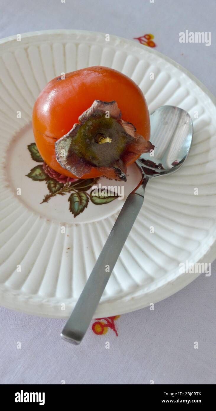 Reife Persimon-Frucht auf dekorierter Untertasse mit Teelöffel - Stockfoto