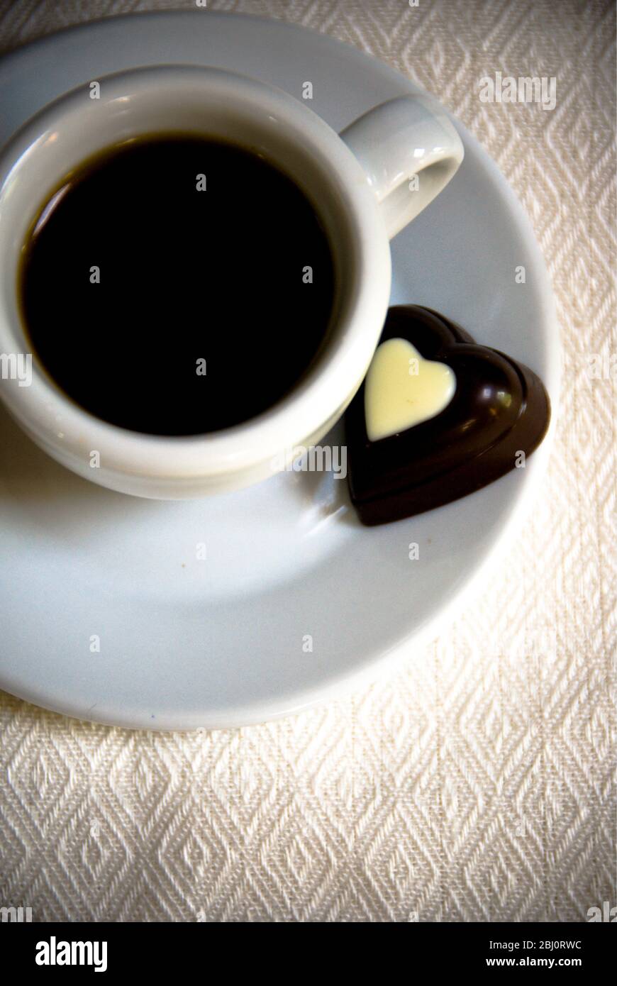 Herzförmige Schokolade auf Untertasse von kleinen Espresso Tasse schwarzen Kaffee - Stockfoto