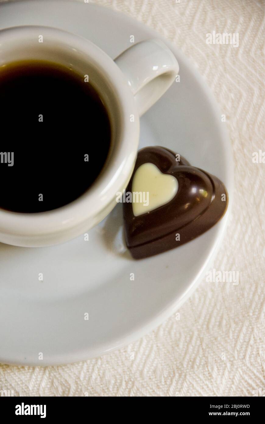 Herzförmige Schokolade auf Untertasse von kleinen Espresso Tasse schwarzen Kaffee - Stockfoto