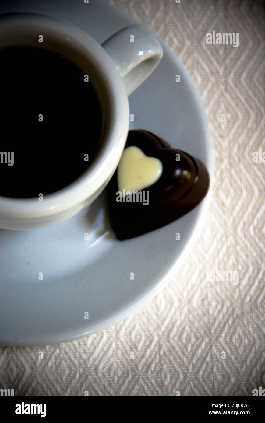 Herzförmige Schokolade auf Untertasse von kleinen Espresso Tasse schwarzen Kaffee - Stockfoto