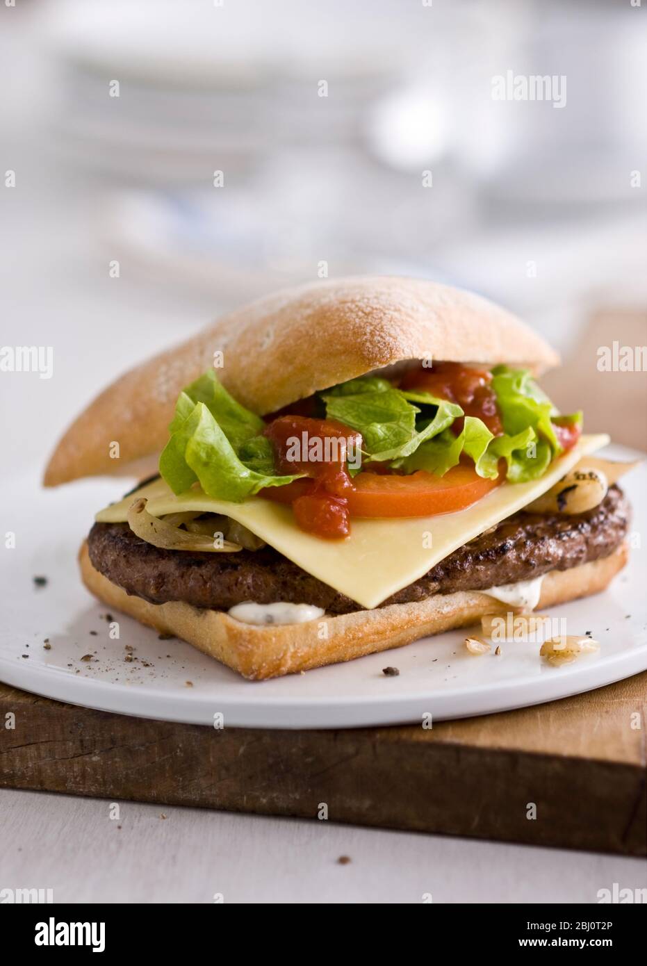 Gournet Cheeseburger mit Salat und Tomaten auf Ciabatta Brötchen auf flachem weißen Porzellanteller. - Stockfoto