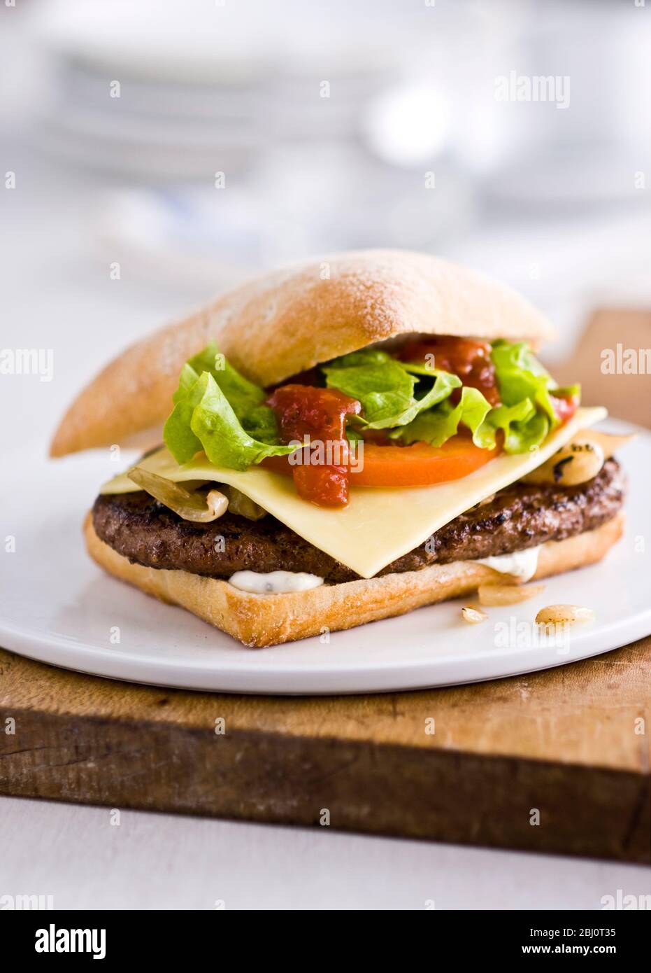 Gournet Cheeseburger mit Salat und Tomaten auf Ciabatta Brötchen auf flachem weißen Porzellanteller. - Stockfoto