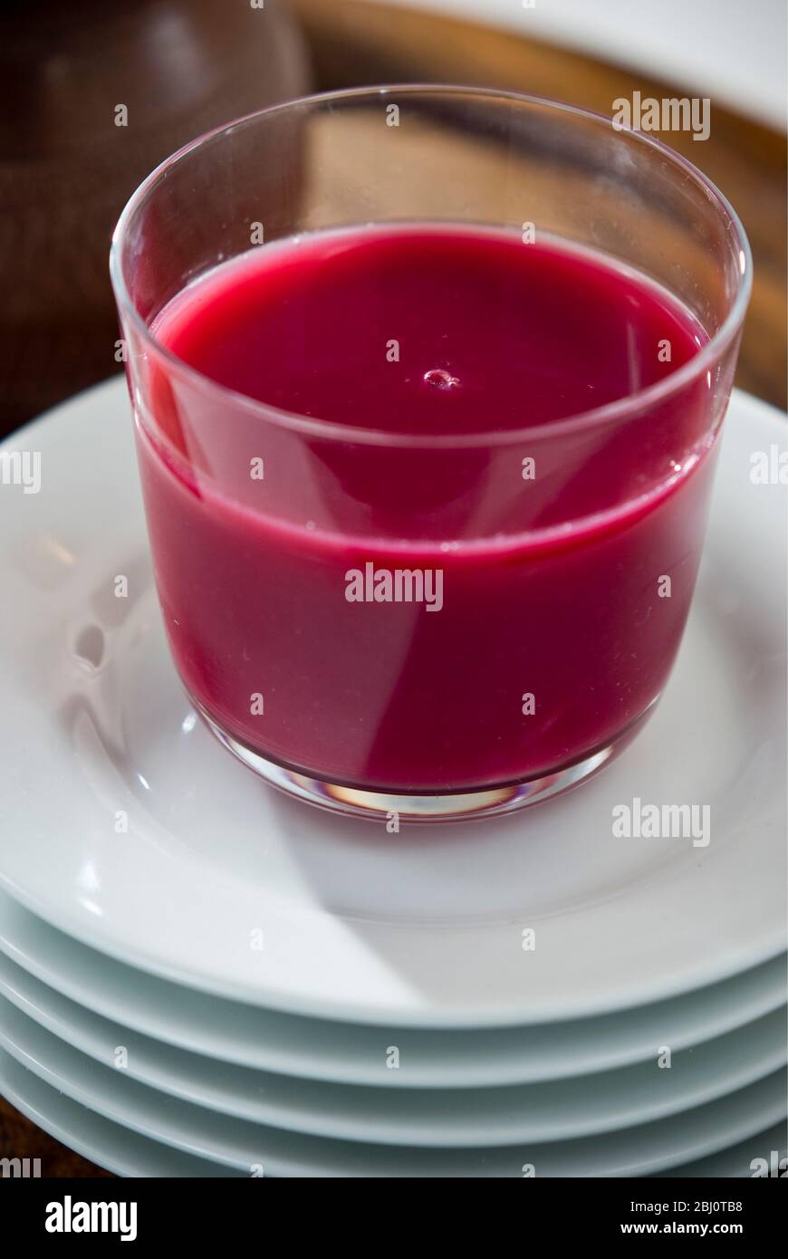 Granatapfelsaft in klarem Glas auf einem Stapel weißer Teller - Stockfoto