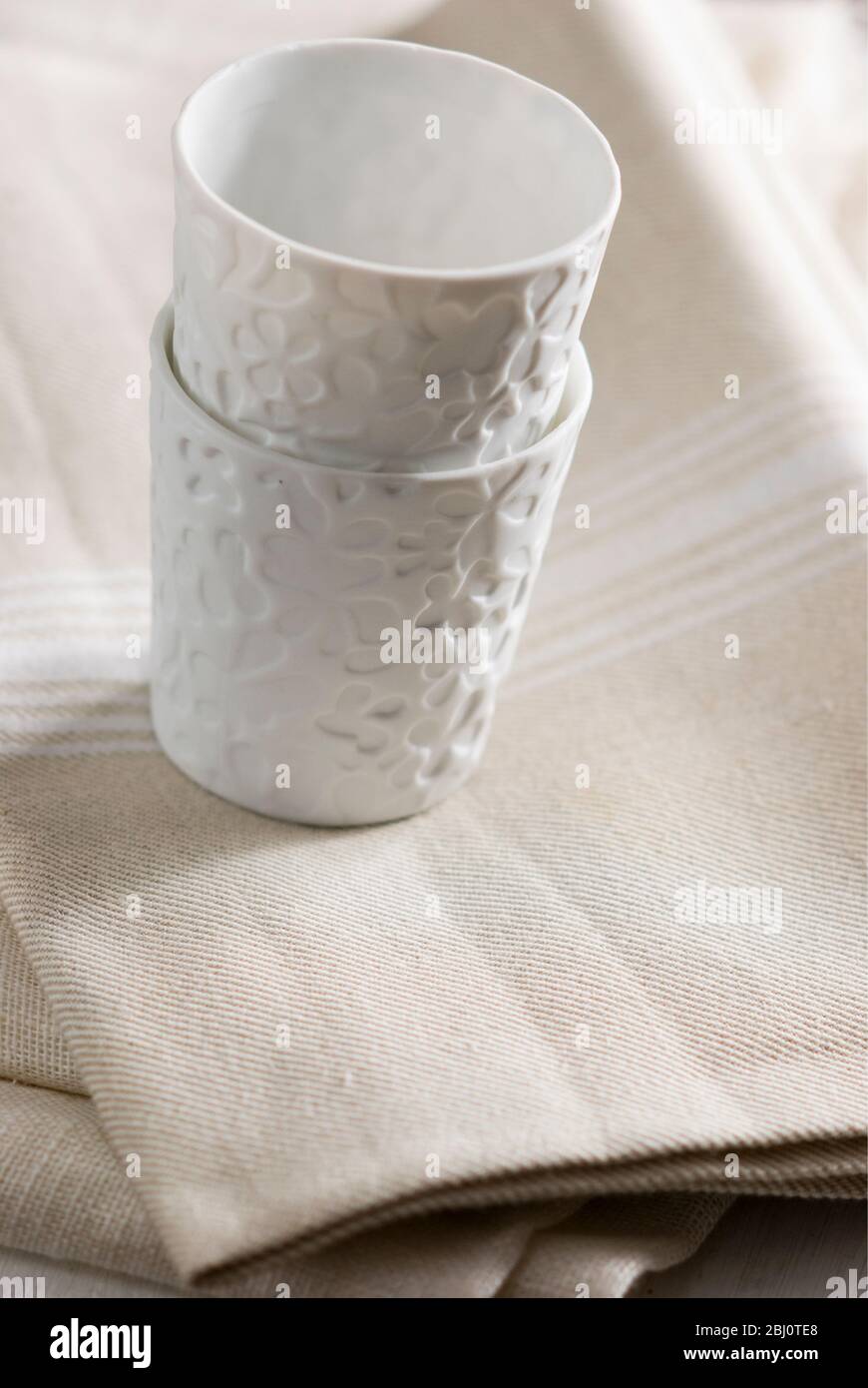 Weiße Porzellanbecher oder Teelicht-Halter auf cremefarbenen Leinentuch gestapelt - Stockfoto