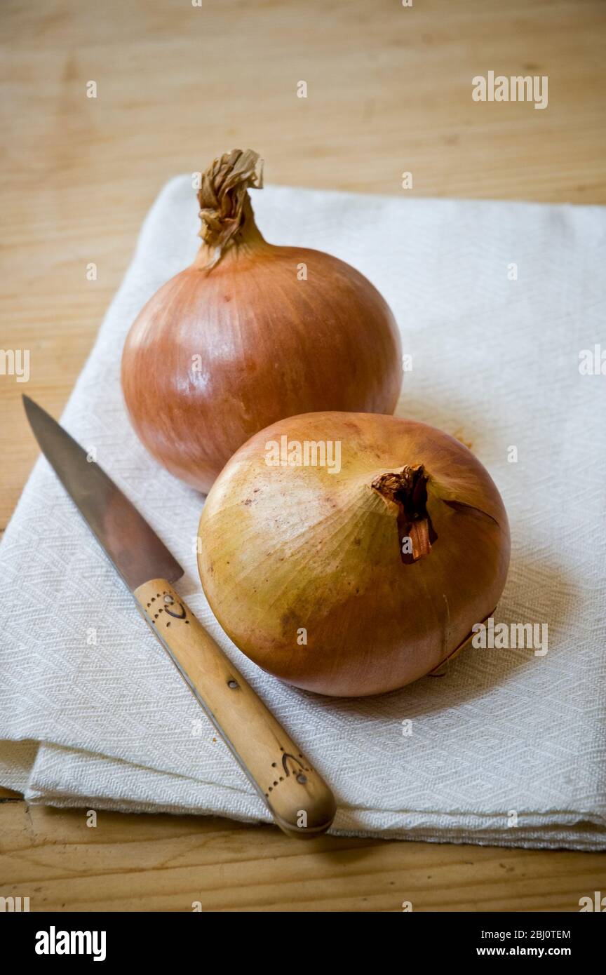 Zwei Zwiebeln auf cremigem weißen Leinentuch mit kleinem französischen Messer - Stockfoto