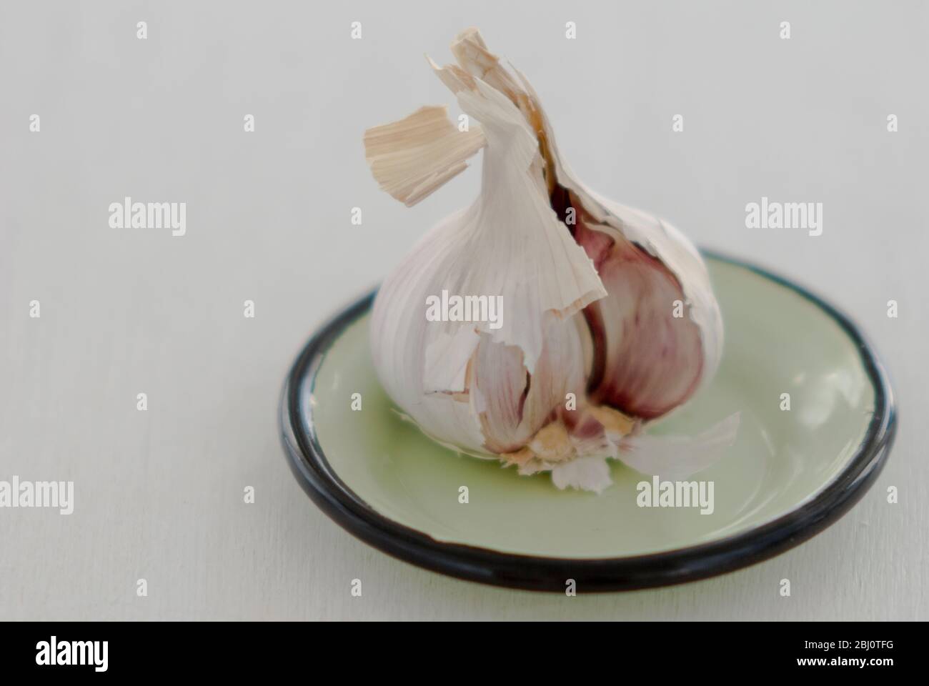 Geöffnet Kopf des Knoblauchs auf kleinen grünen Emaille Untertasse vor weißem Hintergrund - Stockfoto Geöffnet Kopf des Knoblauchs auf kleinen grünen Emaille Untertasse vor weißem Hintergrund - Stockfoto