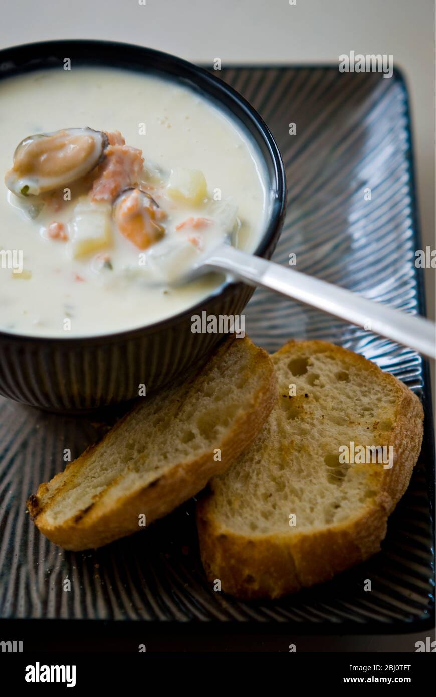 Muschel, Meeresfrüchte und geräucherter Lachs-Chowder in Töpferschüssel mit gegrilltem Brot - Stockfoto